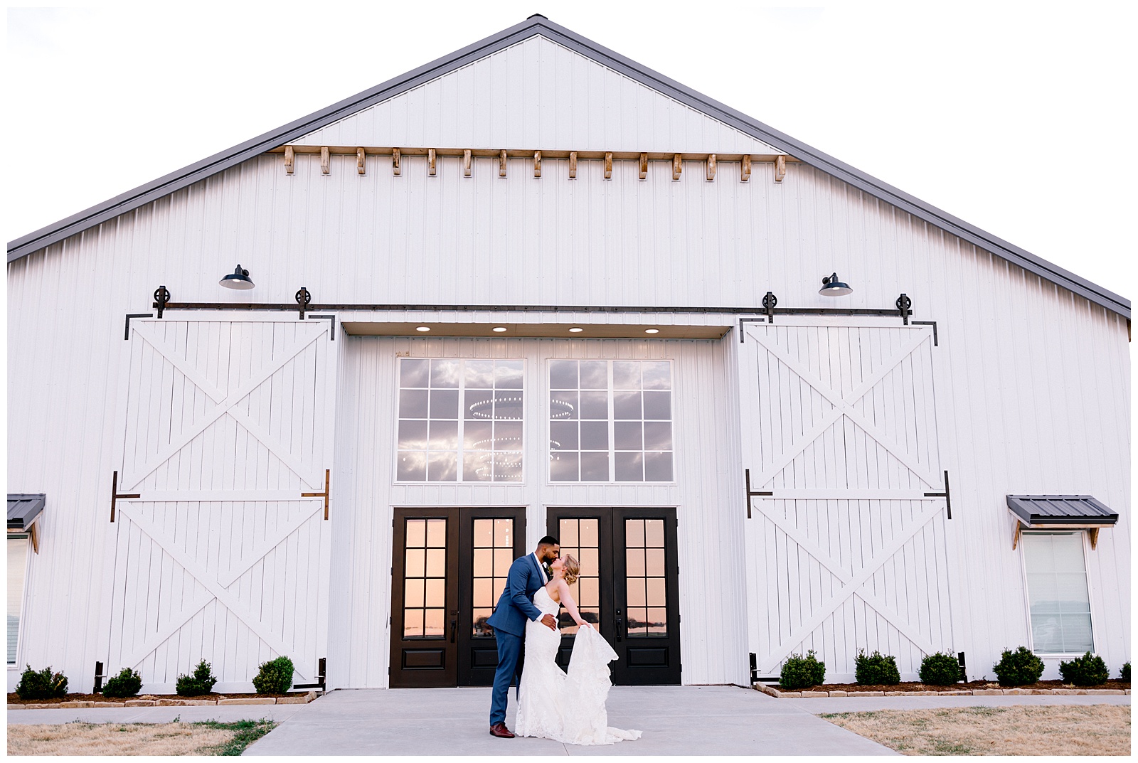 Sunset wedding photo at the barn at grace hill with a couple in wedding attire standing on in front of the barn.